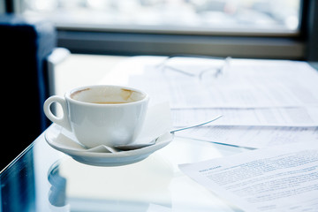 A cup of coffee, eyeglasses and papers lying on the table