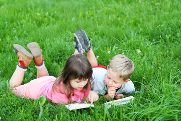 Kids laying on a grass and reading a book together