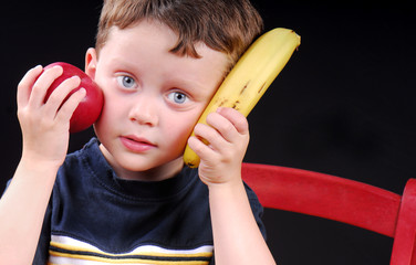 Young boy holding apple and banana