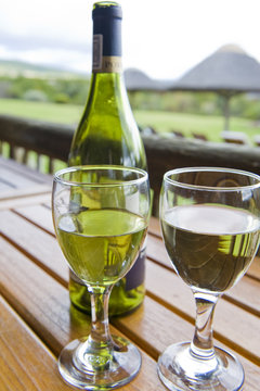 Glasses of white wine on a wooden table outside.