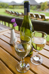 Glasses of white wine on a wooden table outside.