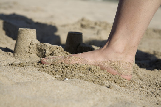 A sand castle at the beach about to be destroyed by a foot