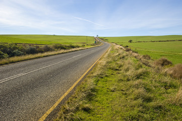 A deserted country road running through some green fields.