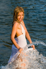 Beautiful girl in a white dress laps in jets of a fountain