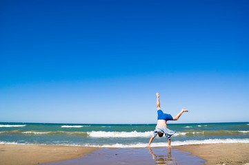 Man up side down. Sand beach and blue water. Summer, vacation.