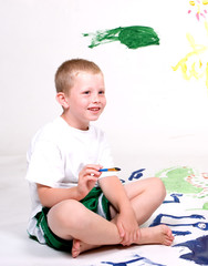 A boy smiles while painting on large white paper.