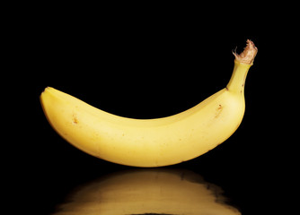 A Banana on black reflective surface.