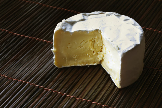 A mini-wheel of creamy brie cheese, on bamboo mat.