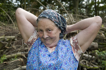 Alte Bäuerin bindet sich das Kopftuch im Wald vor Arbeitsbeginn