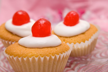 Three iced cup cakes with cherries on top