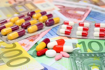 Assorted pills and capsules over euro money.