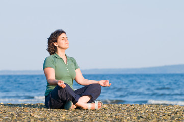 Young brunette woman meditating at the beach sitting on pebbles