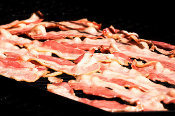 Raw bacon being grilled on an open grittle