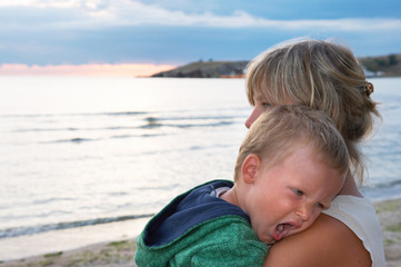 mother with small sleepy boy on evening sandy sea coast