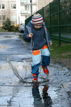 Little boy jumping, splashing and playing in mud pudle.