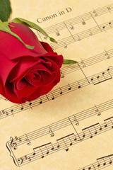 A red rose bud rests on parchment paper sheet music.