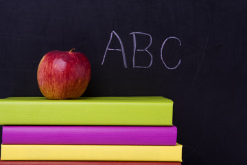apple over a stack of books next to a chalkboard