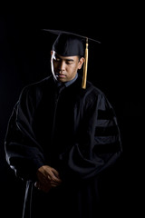 Low key image of a male model in graduation robes and regalia