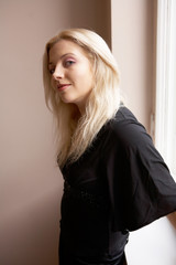 Fototapeta premium Young woman standing beside window, looking at camera