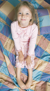 Little girl in pajamas sits on the bed and smiling. Top view.