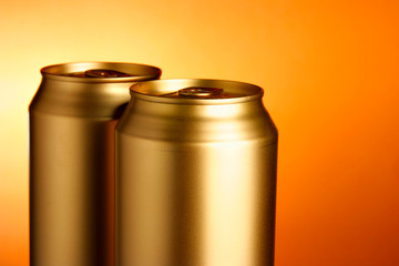 Golden beer cans close-up over orange background