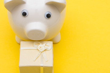 Piggy bank on yellow background with present, holiday savings