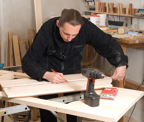Young carpenter making measure with meter in workshop