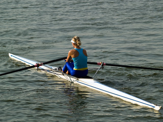 Sporty young lady rowing in boat on water