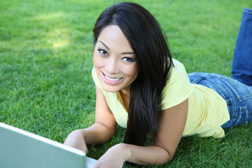 A pretty asian girl working on laptop computer on grass