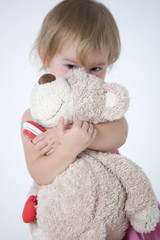 little girl is huging the bear toy and looking