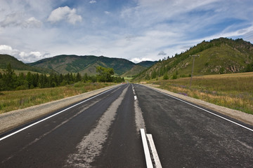 asphalt road among mountains and low cloud sky