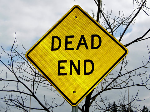 A dead end sign with a defoliated tree in the background