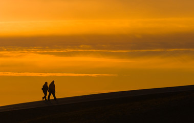 silhouettes of two walking tourists on sunset sky background