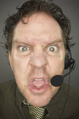 Irate Businessman Wears Phone Headset - Grey Background.