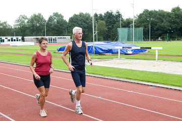 Senior couple running together on a track in a stadium.