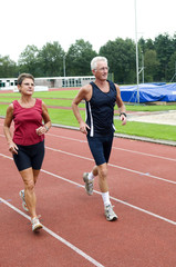 Senior couple running together on a track in a stadium.