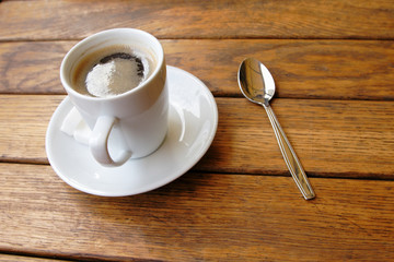 a cup of coffee and teaspoon on the wooden table in cafe
