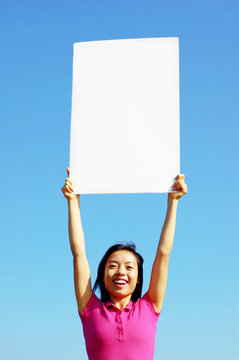 Girl Holding Blank Sign In Front Of Big Blue Sky.