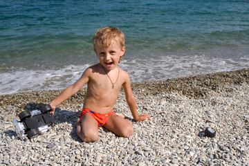 a little white-headed boy plays a toy car on a stony beach