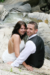 Beautiful bride and groom sitting on a rock by a waterfall.