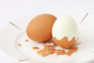 A cooked egg peeled and standing with eggshell pieces.