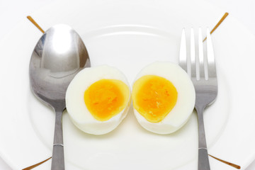 Cooked egg put on white plate with folk and spoon.