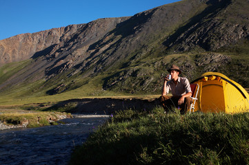 Naklejka premium man is drinking at the camp in mountains near the stream.