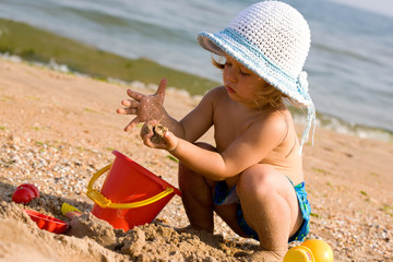 little girl in the bonnet plaing with sand, childhood - obrazy, fototapety, plakaty