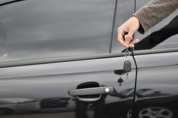 male hand holding car key with new black car in background