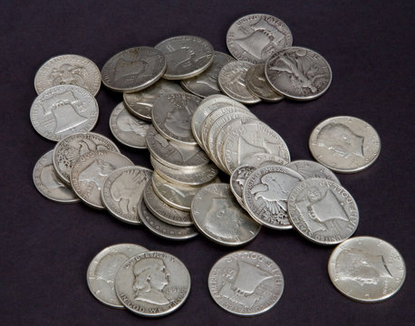 A pile of old silver coins on a black background.