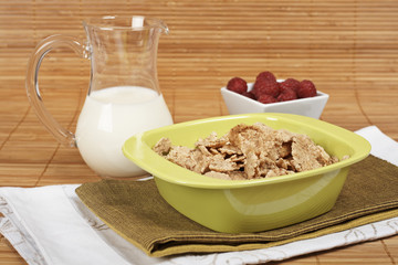 A bowl of cornflakes, milk and raspberries on bamboo mat