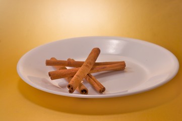Cinnamon sticks on a white plate over a gold background
