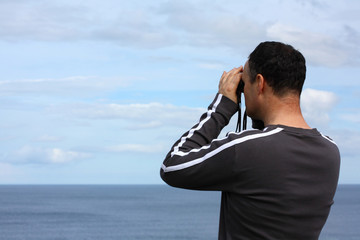 Adult man watching the sea with binoculars