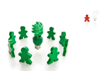 Wooden people around a green compact fluorescent bulb.